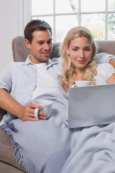 Pareja relajada con tazas de café usando computadora portátil en el sofá — Foto de Stock