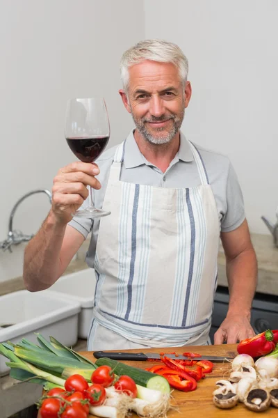 Homem maduro com copo de vinho enquanto corta legumes na cozinha — Fotografia de Stock