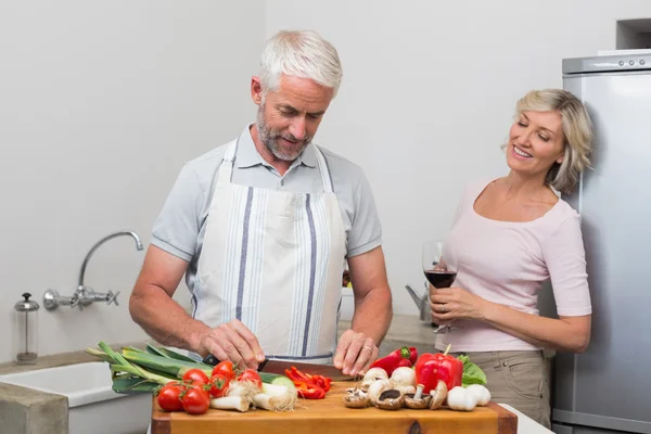 Mann hackt Gemüse, während Frau mit Weingläsern in Küche steht — Stockfoto