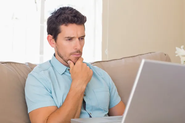 Concentrated man using laptop on couch — Stock Photo, Image