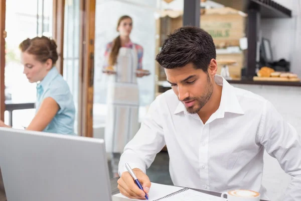 Man skriva noter med laptop i kafé — Stockfoto