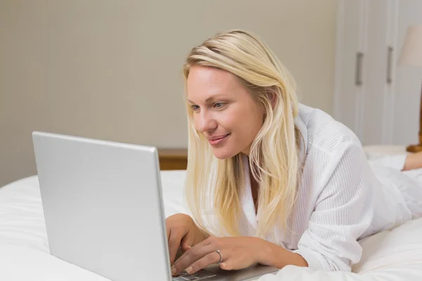 Woman using laptop while lying in bed — Stock Photo, Image