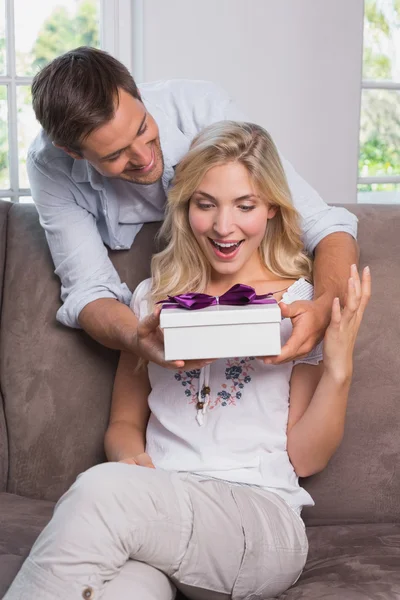 Улыбающийся мужчина удивляет веселую женщину подарком — стоковое фото
