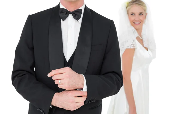 Жених регулирует рукав смокинга, пока невеста смотрит на него — стоковое фото