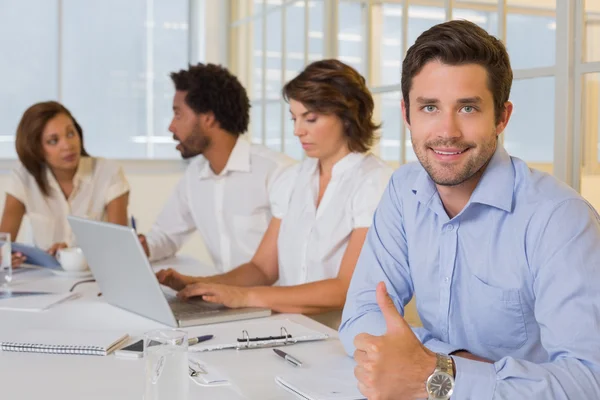 Smiling businessman gesturing thumbs up with colleagues in meeting Stock Image