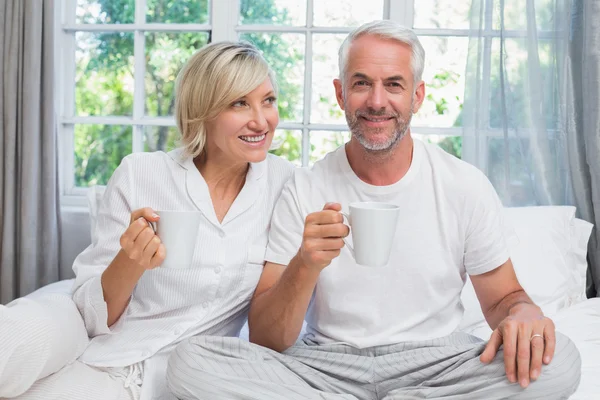 Ouder paar lacht met koffie cups zittend op bed — Stockfoto