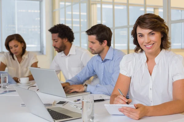 Sonriente mujer de negocios escribiendo notas con colegas en la reunión Imagen de archivo