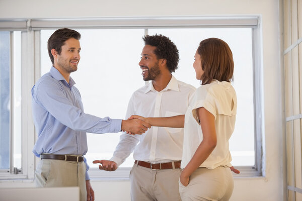 Business people shaking hands besides colleague at office Stock Image