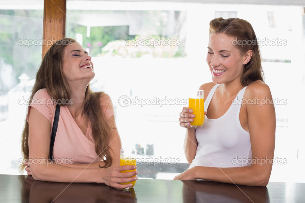 Happy female friends drinking orange juice at cafe