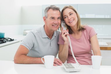 Happy couple using landline phone together in kitchen clipart