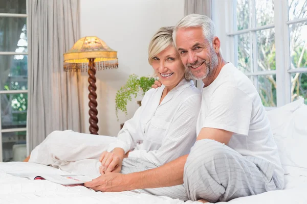 Retrato de um casal maduro feliz relaxado com livro na cama — Fotografia de Stock