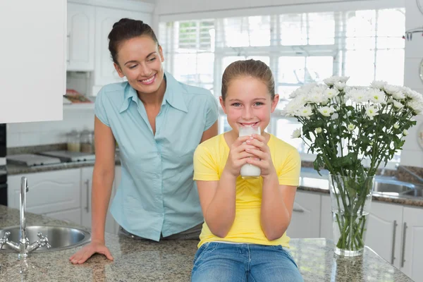 Moeder kijkend meisje consumptiemelk in keuken — Stockfoto