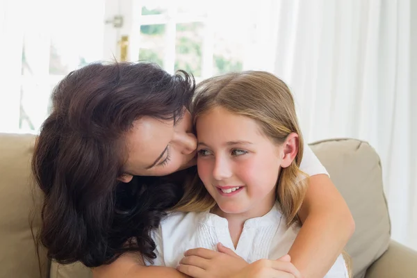 Mother kissing cute daughter on sofa — Stock Photo, Image