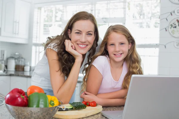 Счастливые мать и дочь пользуются ноутбуком на кухне — стоковое фото