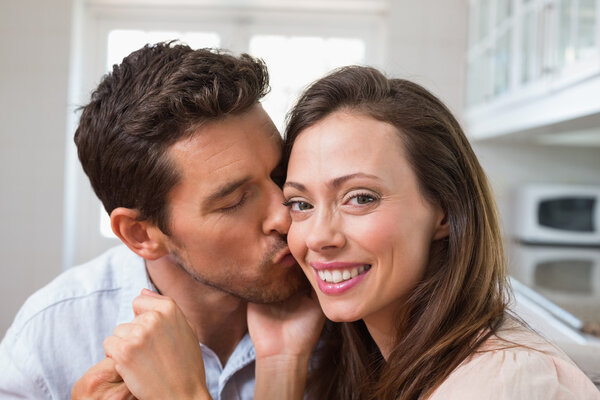 Loving man kissing woman on cheek at home