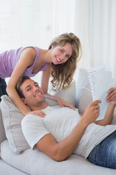 Relaxed young couple reading document on couch — Stock Photo, Image