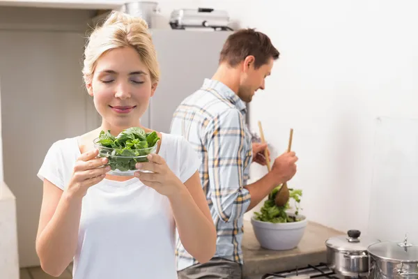 Woman holding bowl of leaves with man preparing salad — Stock Photo, Image