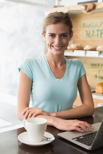 Mulher sorridente com xícara de café usando laptop no café — Fotografia de Stock