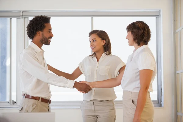Business people shaking hands besides colleague at office — Stock Photo, Image