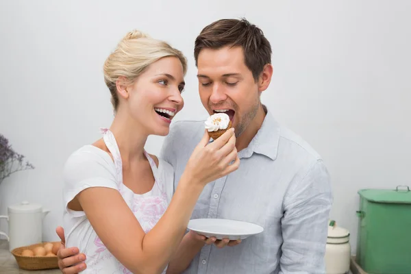 Happy woman feeding man pastry in kitchen — Stock Photo, Image