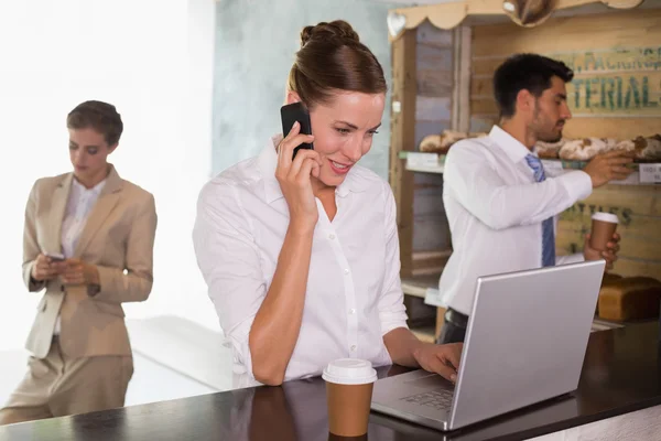 Businesswoman using mobile phone and laptop in office cafeteria — Stock Photo, Image