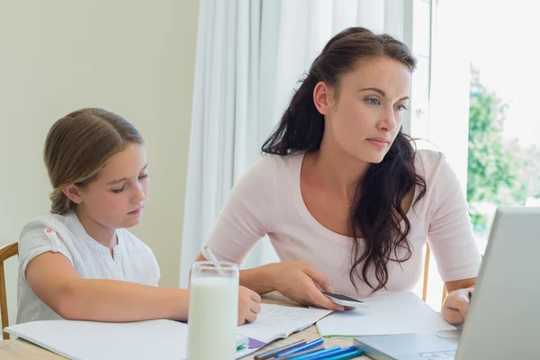 Mujer usando tecnologías mientras hija estudiando en la mesa —  Fotos de Stock