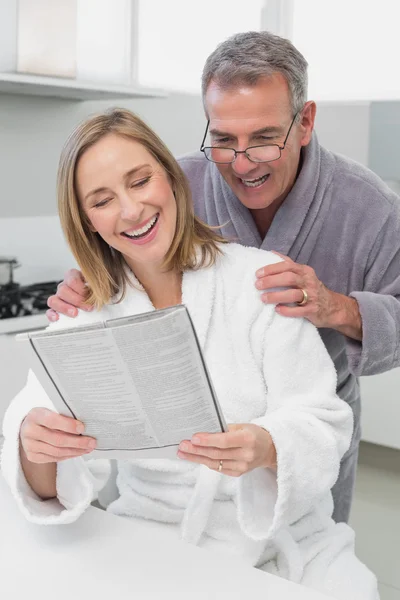 Casal feliz em roupões de banho ler jornal na cozinha — Fotografia de Stock