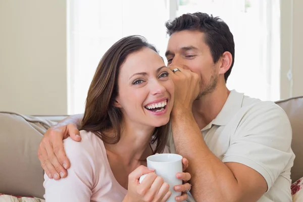 Man whispering secret into a cheerful womans ear in living room — Stock Photo, Image