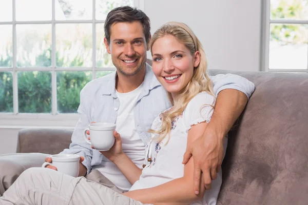 Relaxed loving couple with coffee cups sitting on sofa — Stock Photo, Image