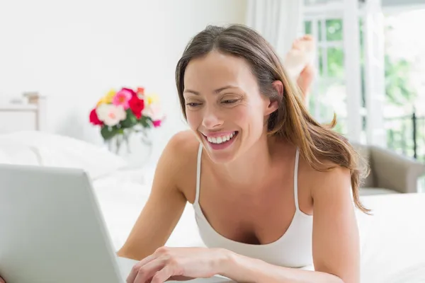 Sonriendo mujer relajada usando el ordenador portátil en la cama —  Fotos de Stock