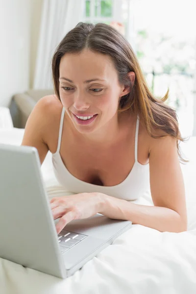 Dizüstü bilgisayar kullanan yatakta rahat kadın gülümsüyor — Stok fotoğraf