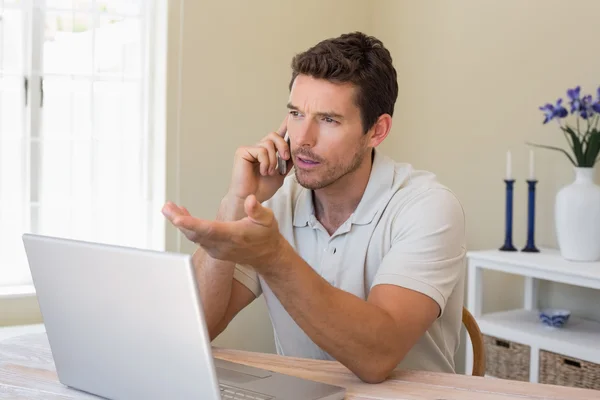 Uomo che utilizza laptop e telefono cellulare a casa — Foto Stock