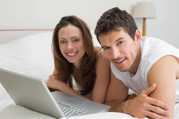 Lachende paar met laptop in bed — Stockfoto