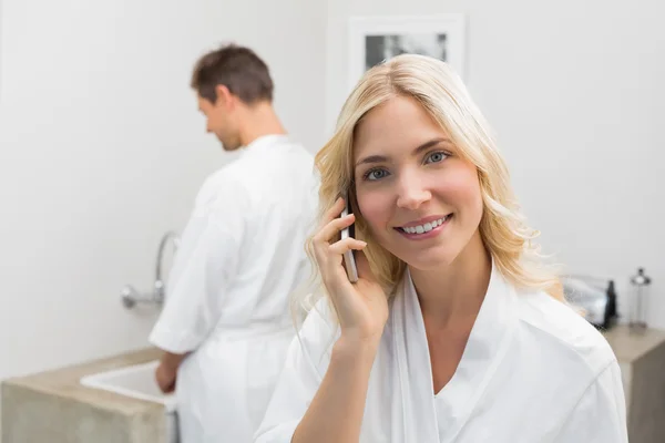 Woman using cellphone with man in background in kitchen — Stock Photo, Image