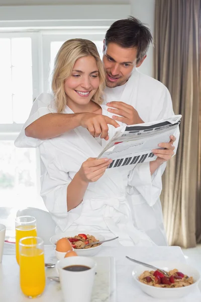 Young couple reading newspaper while having breakfast at home — Stock Photo, Image