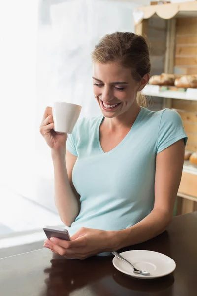 Kvinna dricker kaffe medan du använder mobiltelefon vid disken i kafé — Stockfoto