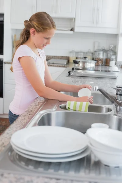 Vista lateral de una niña utensilios de lavado en la cocina — Foto de Stock