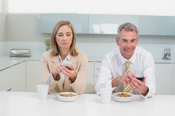 Couple d'affaires messagerie texte tout en prenant le petit déjeuner dans la cuisine — Photo