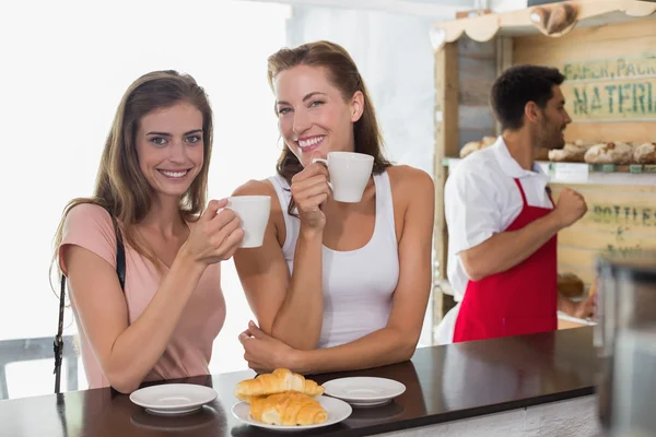 Mujeres sonrientes tomando café con barista en segundo plano en la cafetería —  Fotos de Stock