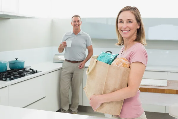 Woman carrying grocery bag while man with coffee cup in kitchen — Stock Photo, Image