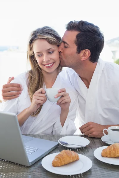 Mann küsst Frau, während er Laptop auf Frühstückstisch benutzt — Stockfoto