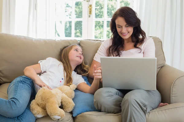 Woman using laptop by daughter on sofa — Stock Photo, Image