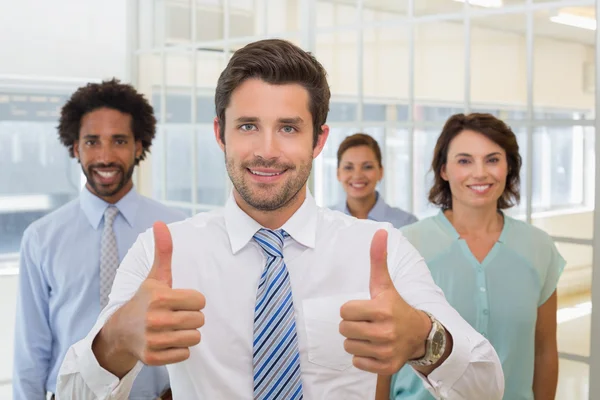 Businessman with colleagues gesturing thumbs up in office — Stock Photo, Image
