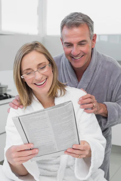 Szczęśliwa para w szlafroki czytanie gazety w kuchni — Zdjęcie stockowe
