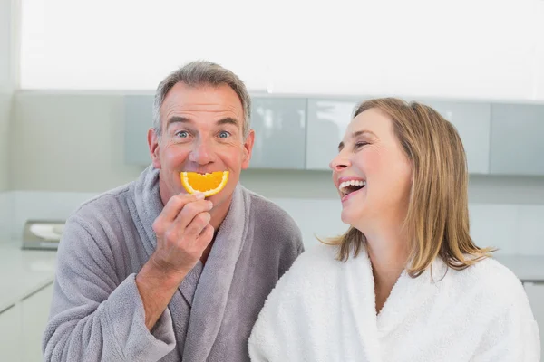 Portrait of a cheerful couple with orange slice in kitchen — Stock Photo, Image