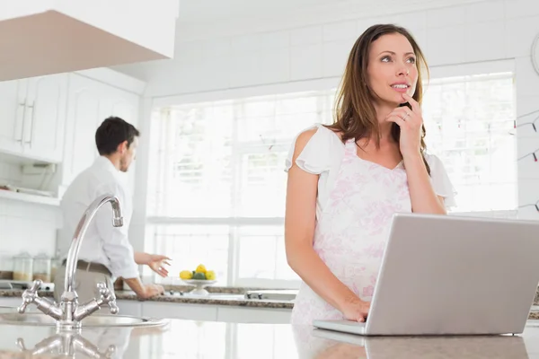 Mulher usando laptop com homem no fundo na cozinha — Fotografia de Stock