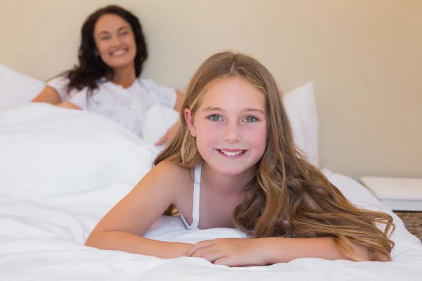 Girl lying in bed with mother in background — Stock Photo, Image