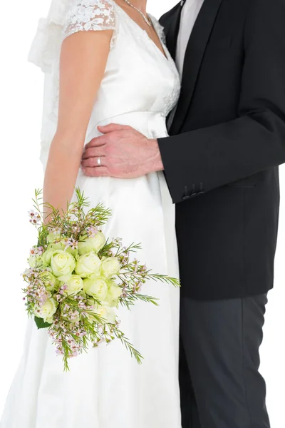 Bride holding flower bouquet while embracing groom — Stock Photo, Image