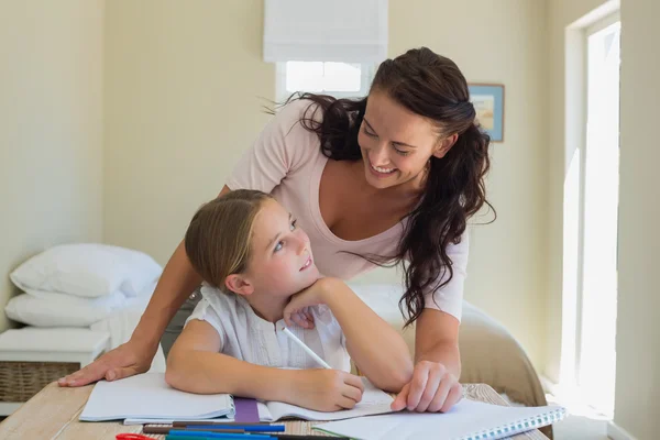 Madre mirando a su hija haciendo la tarea en la mesa — Foto de Stock