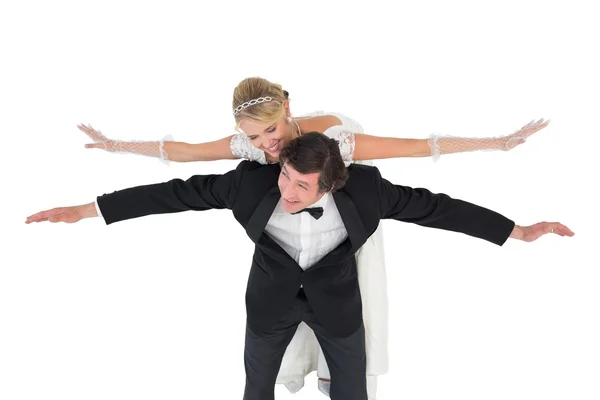 Happy groom with arms outstretched carrying bride on back — Stock Photo, Image
